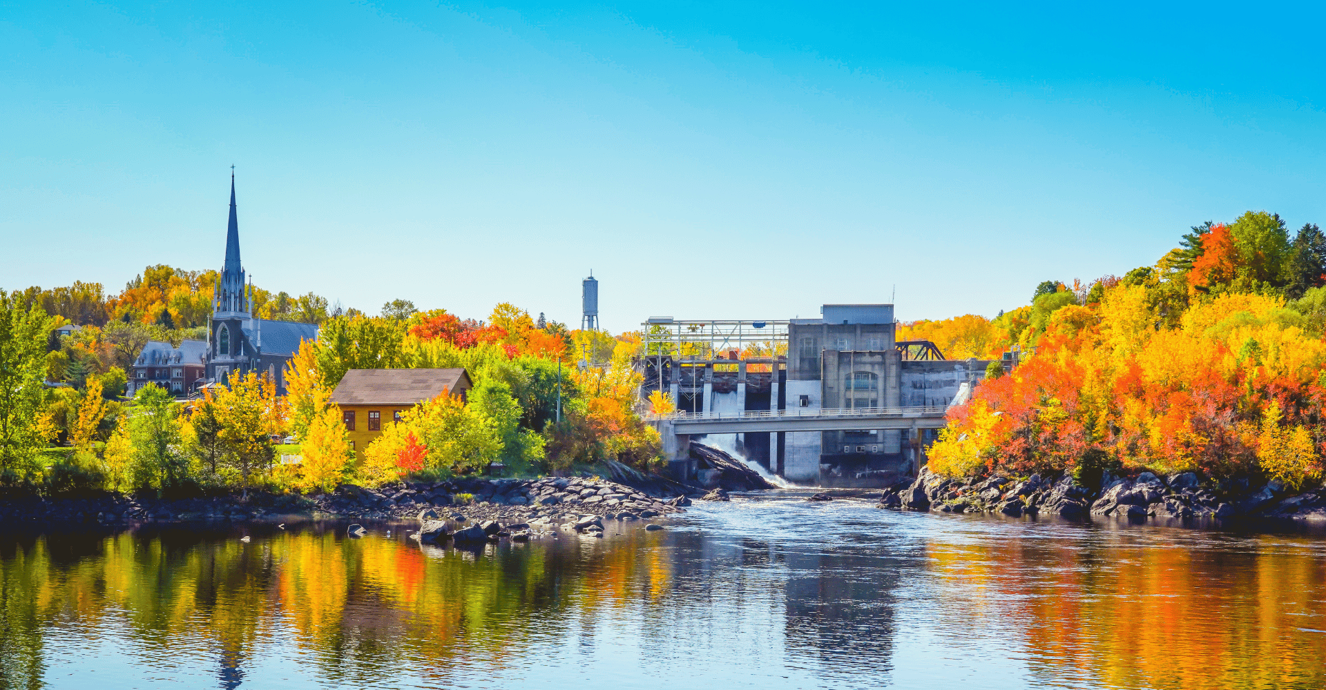 Commercial Real Estate Market of the Month: Chicoutimi 4 Autumn Landscape View of Color Trees with Dam and Chruch in Fall Season in Chicoutimi the city experiencing an industrial real estate shift.